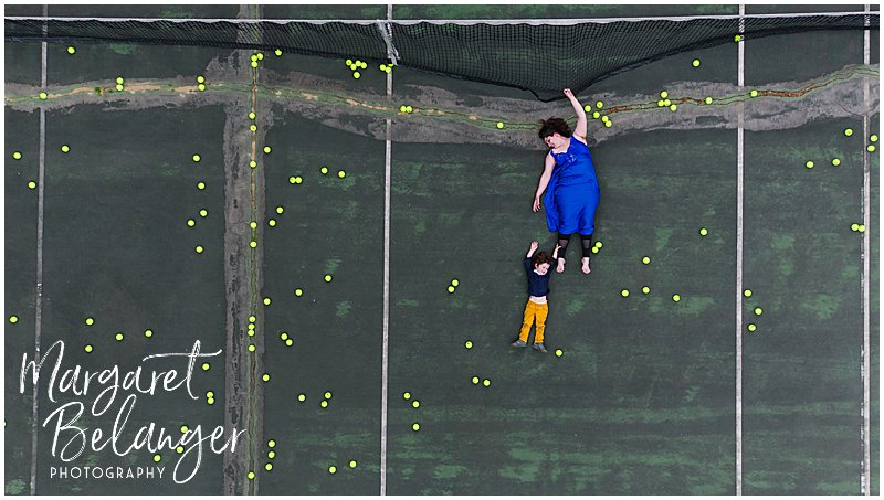 Drone portrait of a woman and a little boy hanging from the net on a tennis court