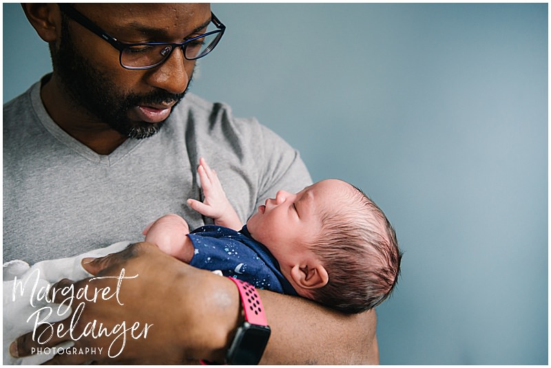 Dad cradles newborn son in front of a blue wall