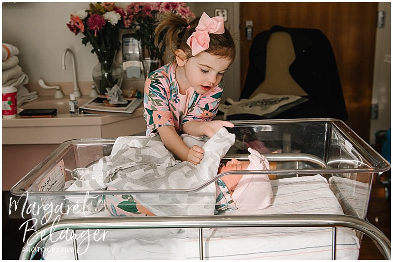 Toddler big sister peering into the bassinet to see her newborn baby sister