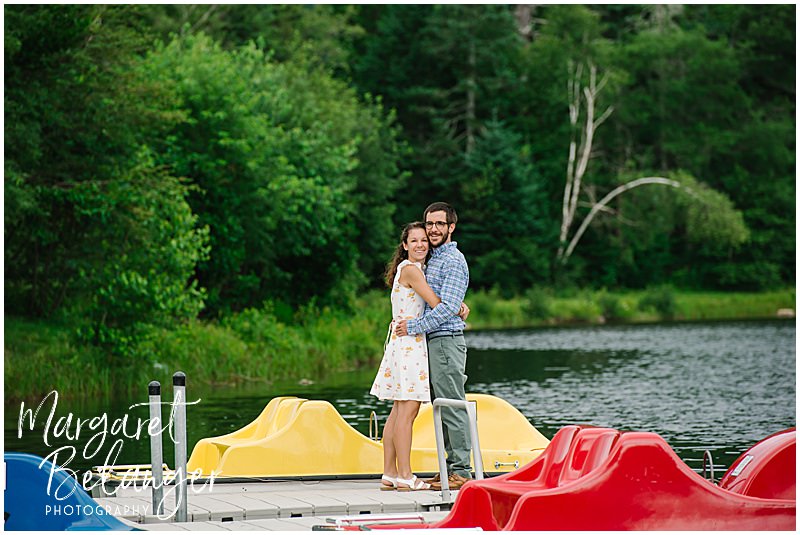 Couple hugging on a dock among colorful paddle boats at Waterville Valley
