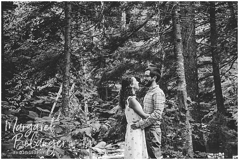 Couple stands among the tall trees by the river at Waterville Valley Resort