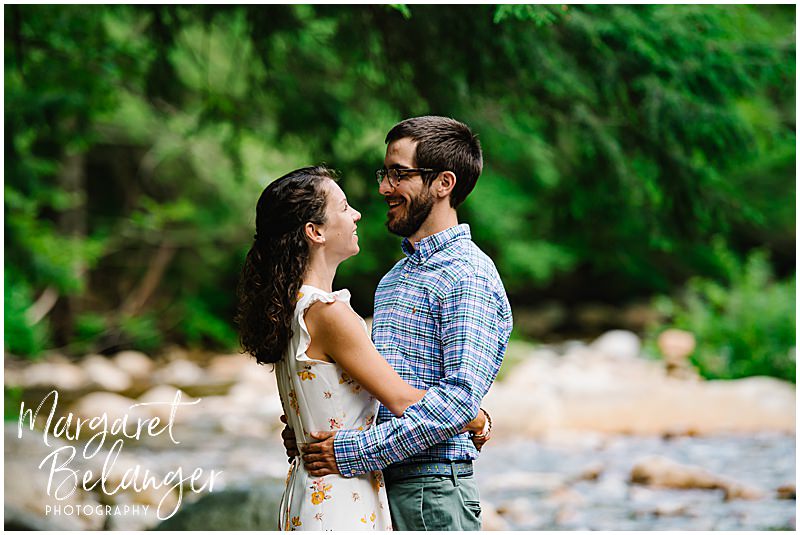 Couple hugs while standing on rocks across the river at Waterville Valley Resort