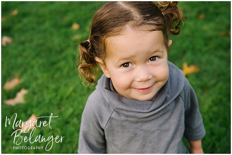 Photo of a little girl in pigtails looking up at the camera during a fall family session at Endicott Park in Danvers.