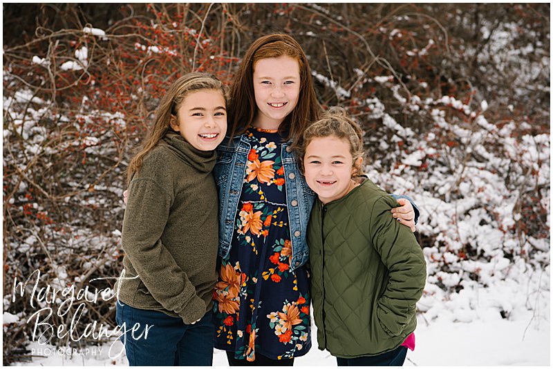Three sisters huddle together and smile for the camera at their winter family session at Minute Man National Park in Lincoln.