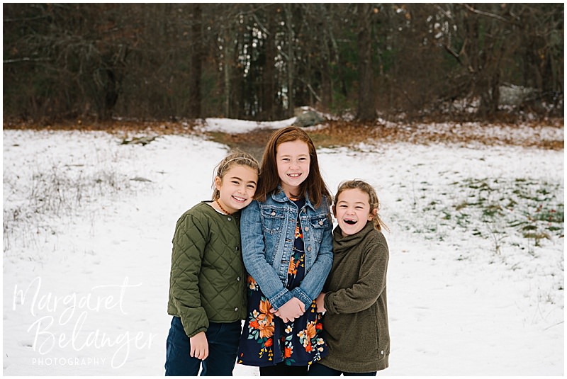 Three sisters standing together in the snow during their winter family session at Minute Man National Park in Lincoln.