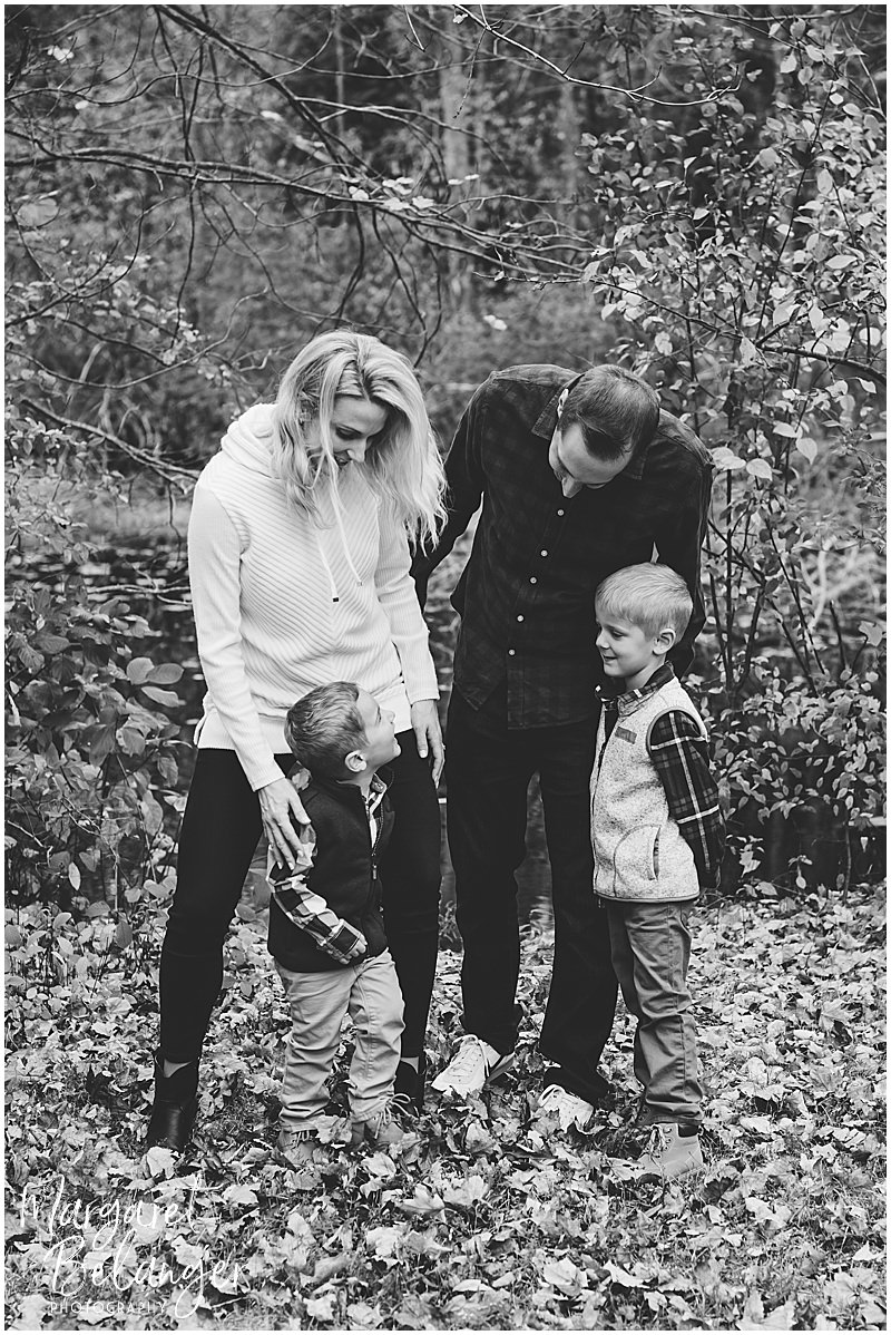 Black & white photo of Mom and Dad with their two little boys standing in the leaves at Minute Man National Park, Lincoln