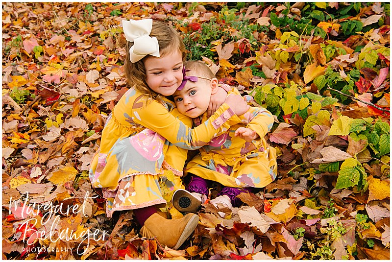 Two little girls hug in the leaves at Mistletoe Christmas Tree Farm in Stow.