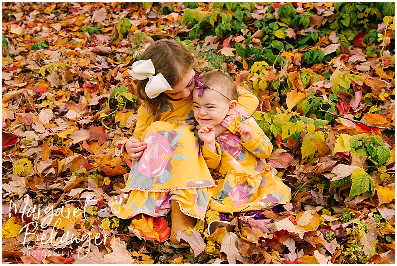 Two little girls hug in the leaves at Mistletoe Christmas Tree Farm in Stow.