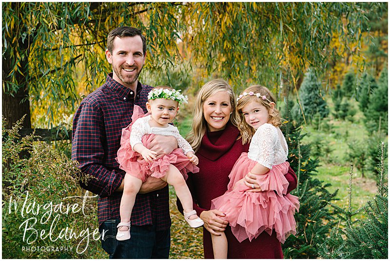 Mom and Dad with their two daughters, both wearing tutus, during their fall family session at Mistletoe Christmas Tree Farm in Stow.