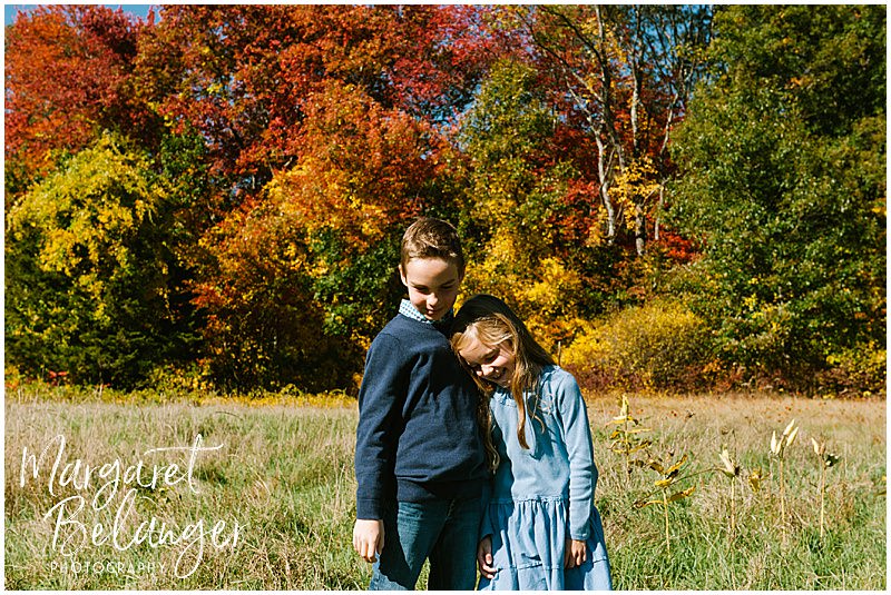 Two little kids hug with bright foliage behind them at Minute Man National Park in Lincoln during their fall family session.