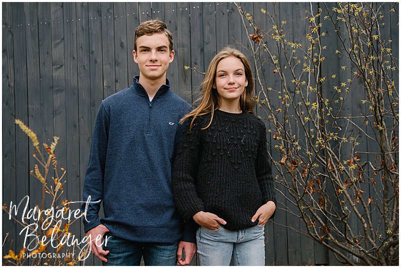 Teenaged siblings posing in front of their gray fence during a Newton family session.