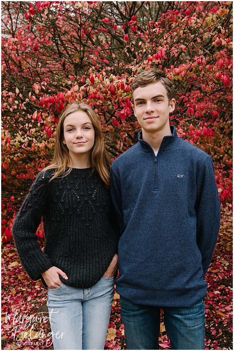 Teenage siblings pose in front of a red tree during their Newton backyard family session.