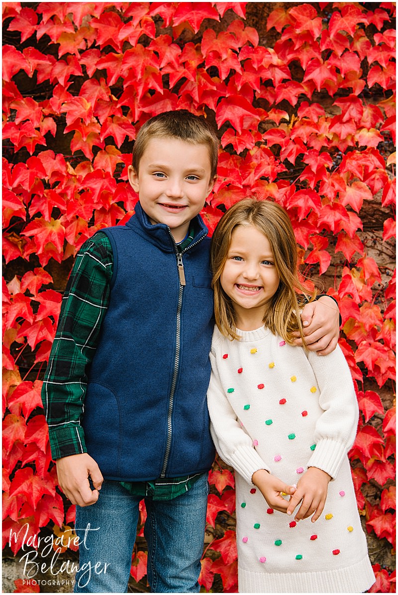 Little girl and her brother in front of a wall of red leaves during their Winchester Center fall family session.