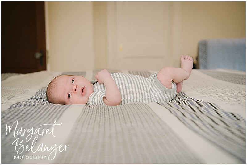 A baby boy lies on a big bed during his newborn photography session in Winchester, MA