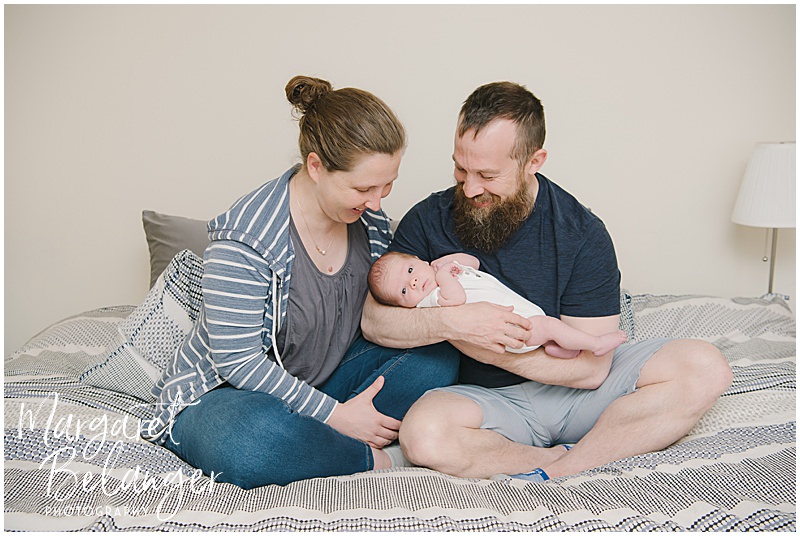 Mom and Dad on the bed holding their newborn son during their newborn photo session in Winchester, MA