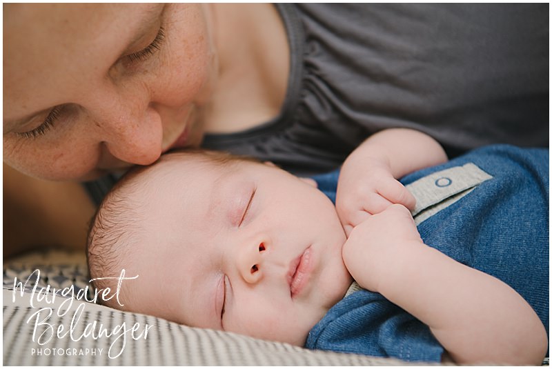 Baby asleep on the bed and mom leans in to kiss him during a Winchester, MA newborn session