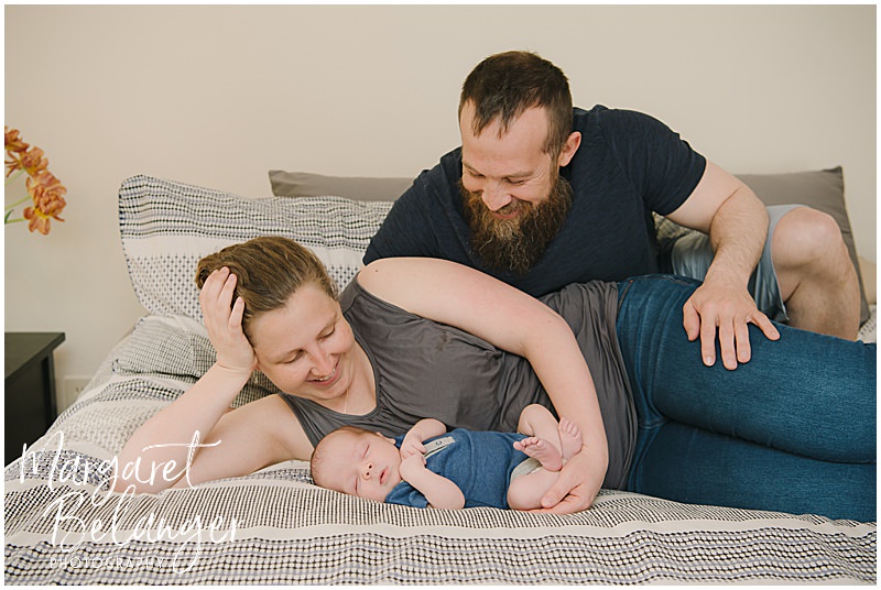 Mom and dad lie on the bed with their newborn baby at their newborn photo session in Winchester, MA.