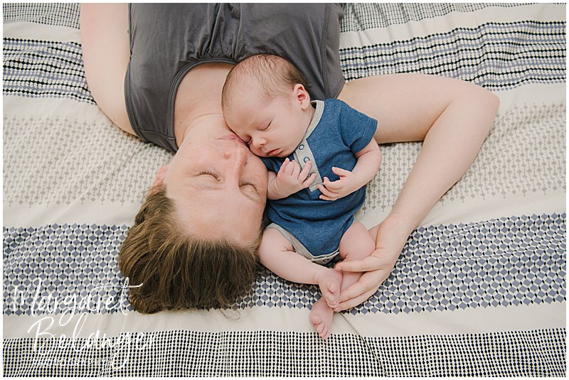 Mom lies on a bed with her newborn baby boy curled up to her during their Winchester, MA newborn session