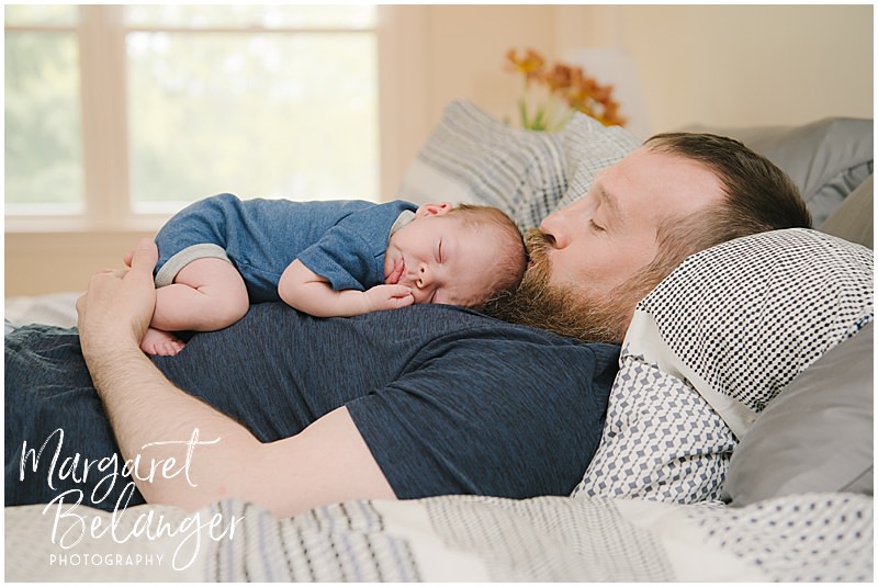 Newborn baby boy lies on top of dad and dad kisses his head during their Winchester, MA newborn session