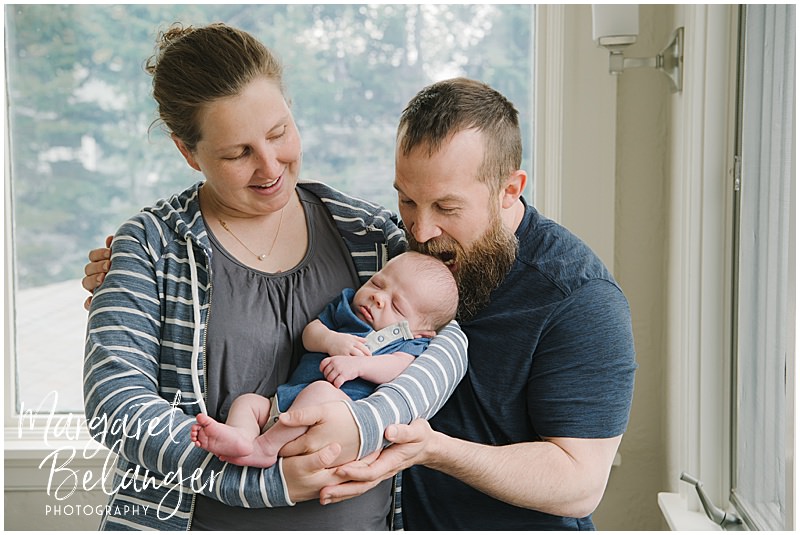 Mom holds baby while Dad pretends to bite baby's head during a Winchester, MA newborn session