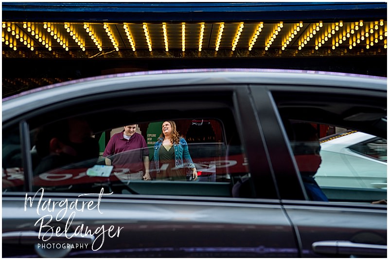 Photo through the windows of a passing car of a laughing couple outside the Paramount Theater in Boston's Theater District.