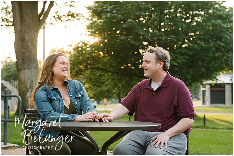 A couple sits at a Boston Common cafe table and laughs together during their engagement session.