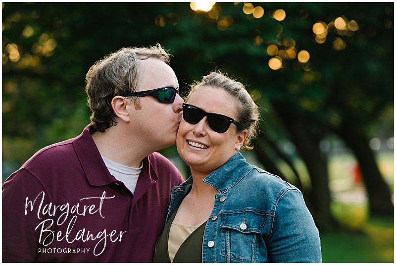 A man in sunglasses kisses his fiancee's cheek during their Boston Common engagement session.