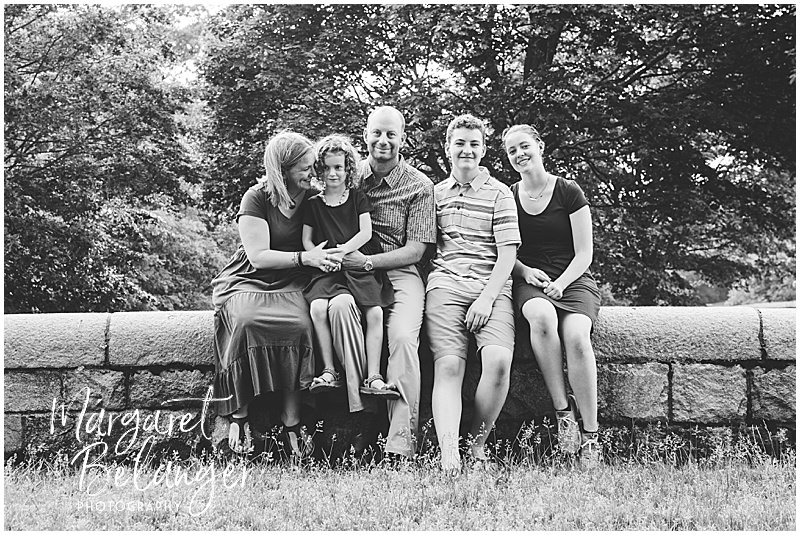 Black and white photo of a family of five sitting on a stone wall at Larz Anderson Park in Brookline.