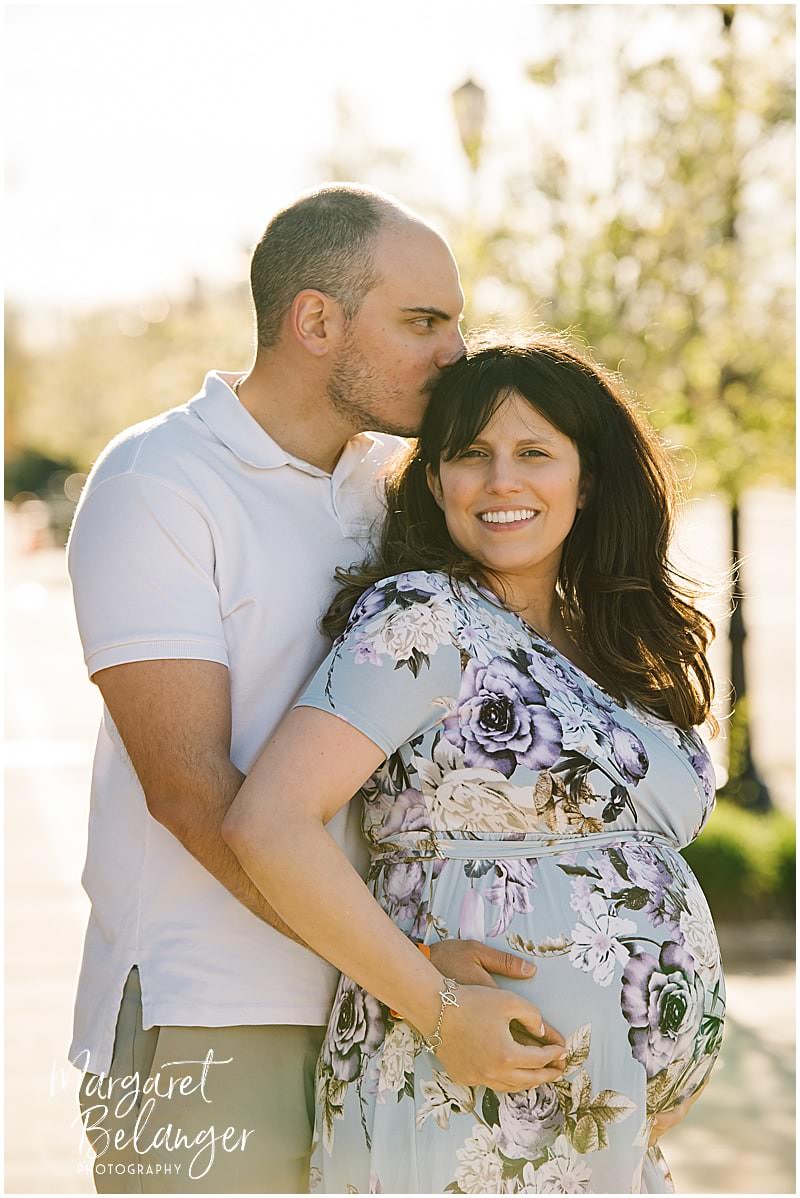Man wraps his arms around his pregnant wife and kisses her on the head during a maternity session in Norfolk, MA.