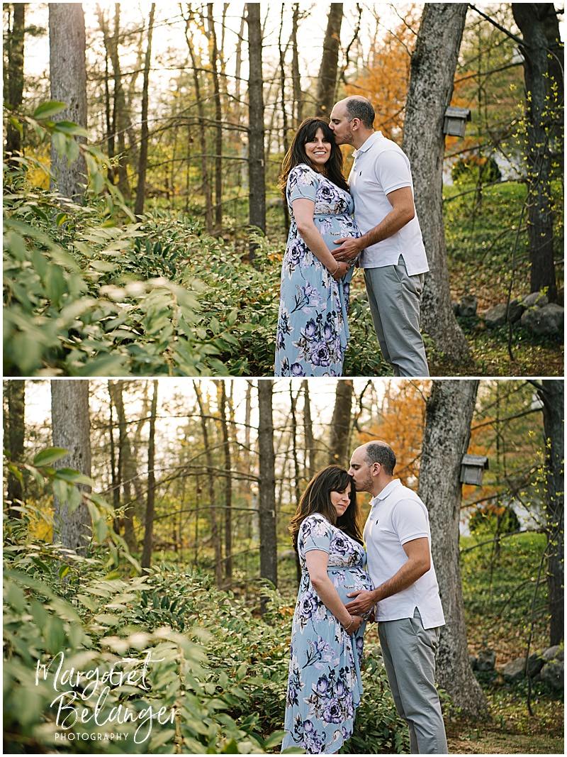 A couple poses among the trees, the man kissing his wife's head, during their Norfolk, MA maternity session.