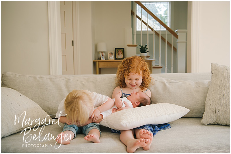 Two little sisters comfort their newborn baby brother on the couch.