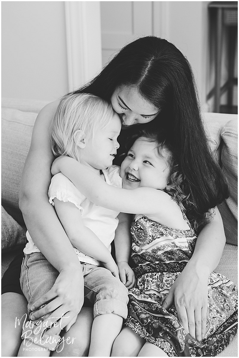 Black and white photo of Mom snuggling her two daughters on her lap.