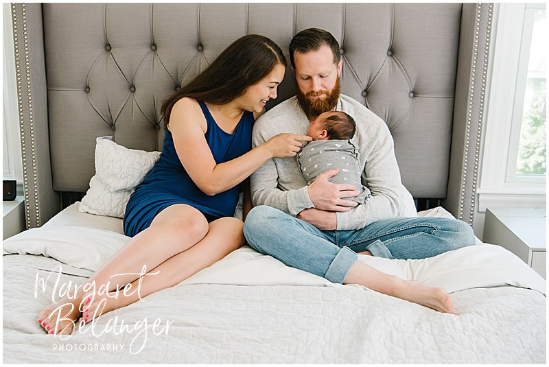 Mom and Dad sit on the bed and hold their newborn son during their at-home Winchester newborn session.