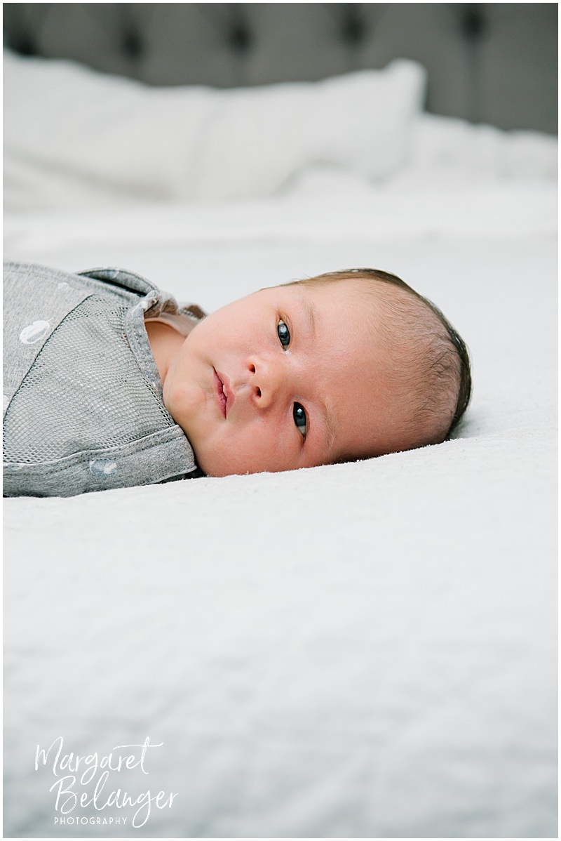Portrait of a newborn baby boy staring at the camera while he's swaddled and lying on his parents' bed.