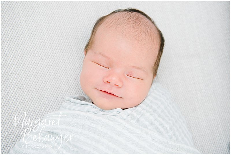A sleeping newborn baby boy manages a tiny smile.
