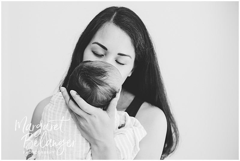 Black and white photo of mom holding her newborn baby boy and giving him a kiss on his cheek.
