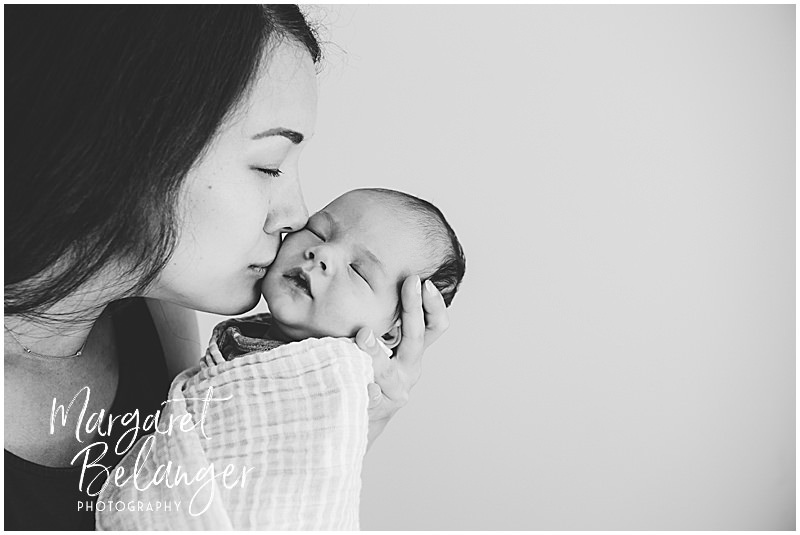 Black and white photo of mom holding her newborn baby boy and giving him a kiss on his cheek.