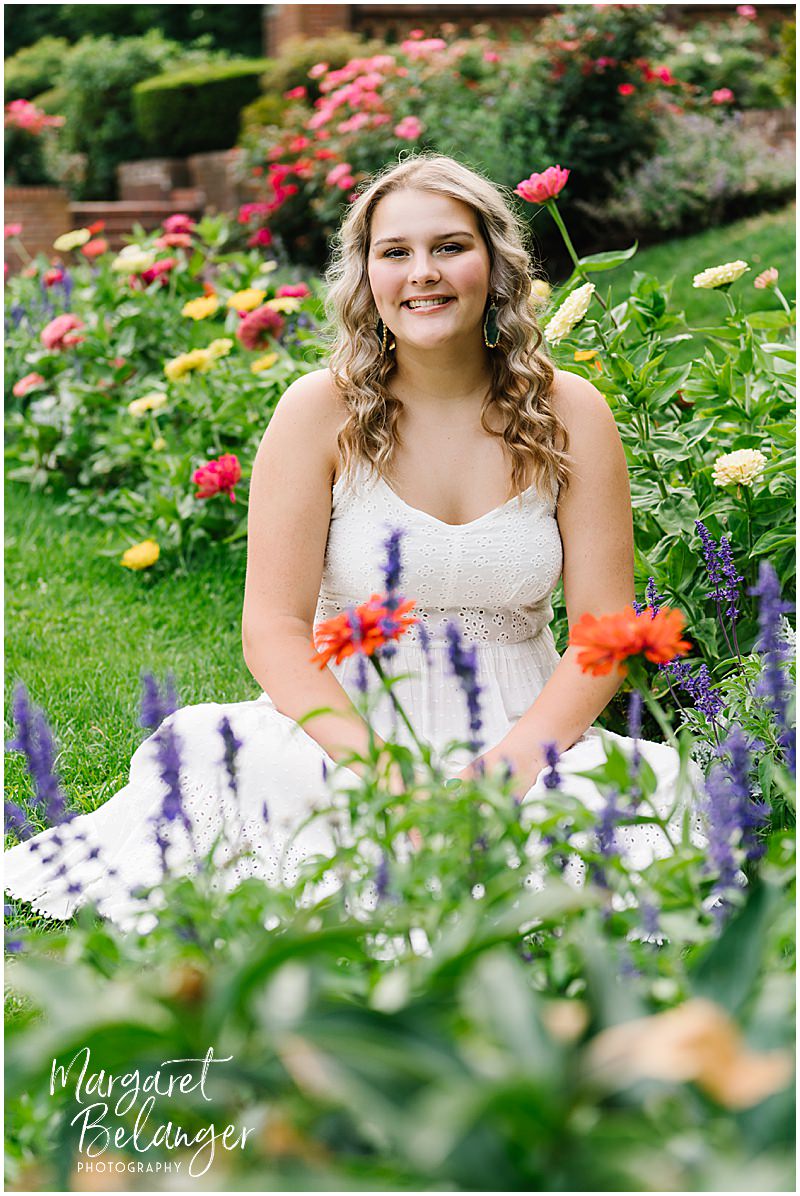 A young woman sits among flowers in a garden.