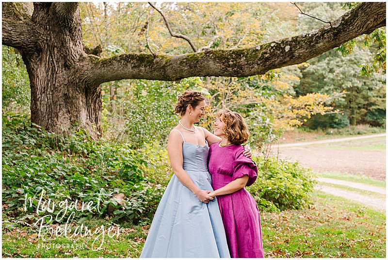 Two brides look at each other by a giant tree at Allandale Farm