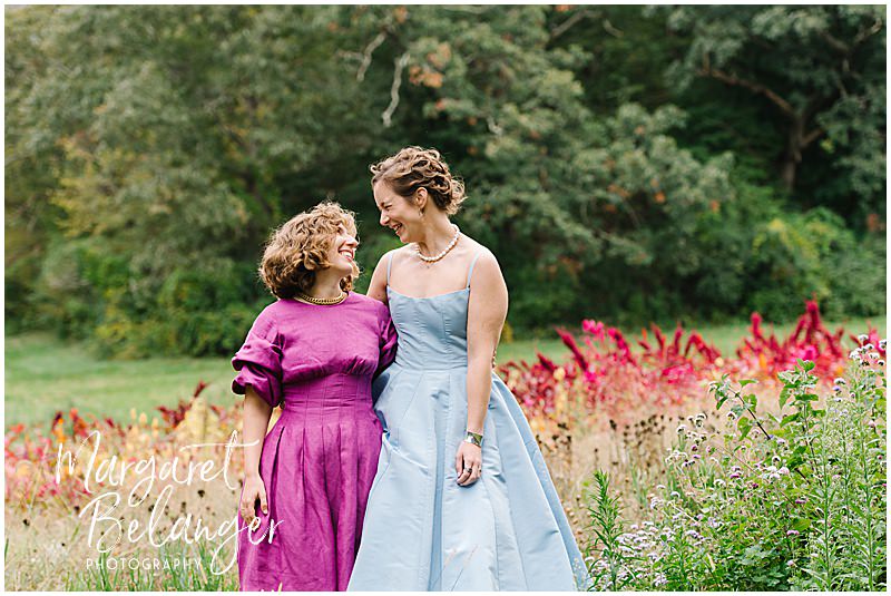 Two brides smile at each other among the flower fields at Allandale Farm in Brookline