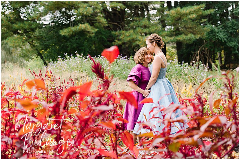 Brides stand among the red flowers at Allandale Farm before their same-sex wedding ceremony