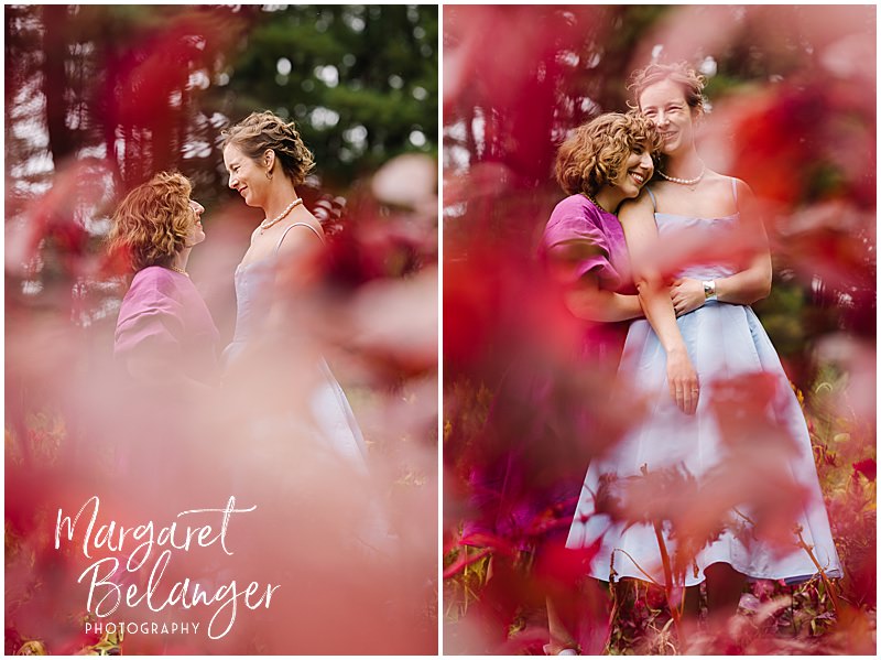 Red flowers frame two brides as they pose among flowers at Allandale Farm