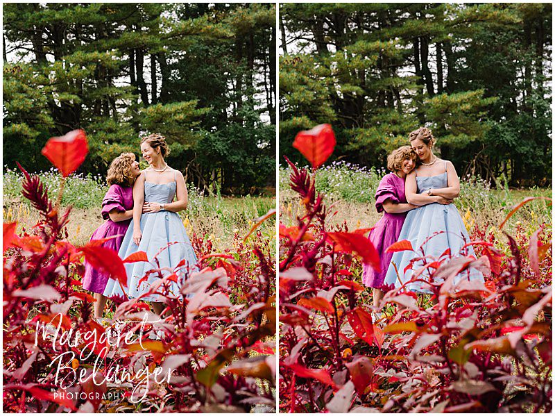 Red flowers frame two brides as they pose among flowers at Allandale Farm in Brookline