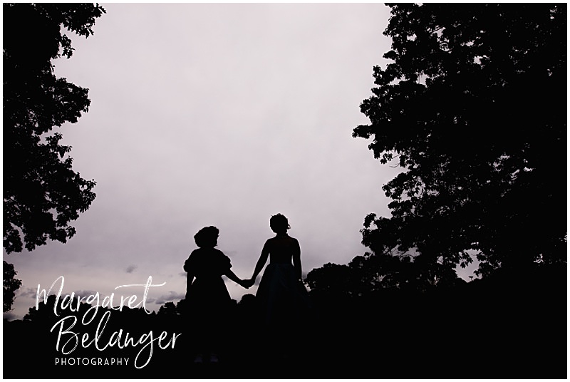 Two brides holding hands silhouetted against a cloudy sky.
