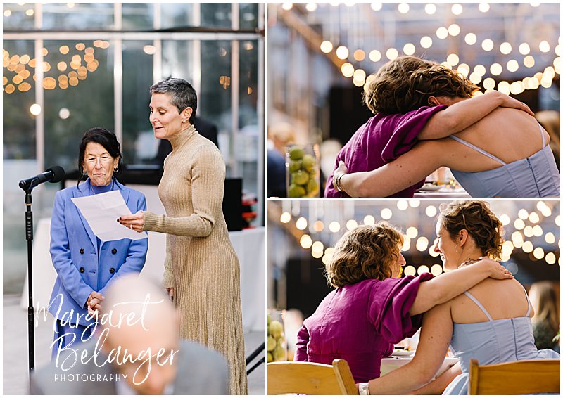 Brides hug while listening to their moms give a toast during their greenhouse wedding reception.