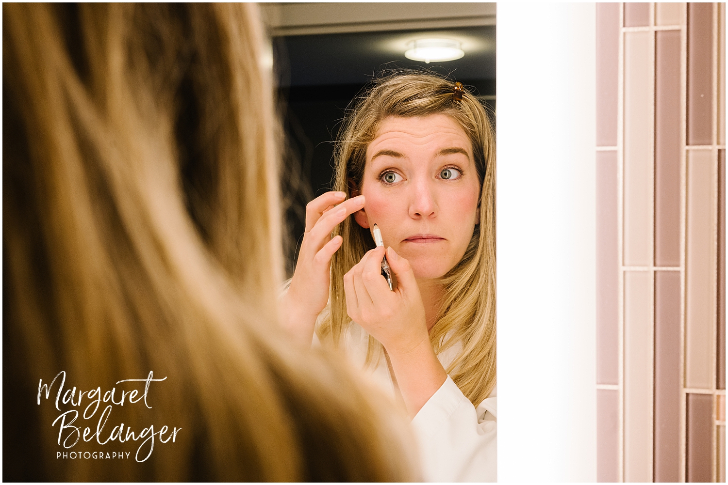 Bride's sister applying makeup while looking into a mirror.