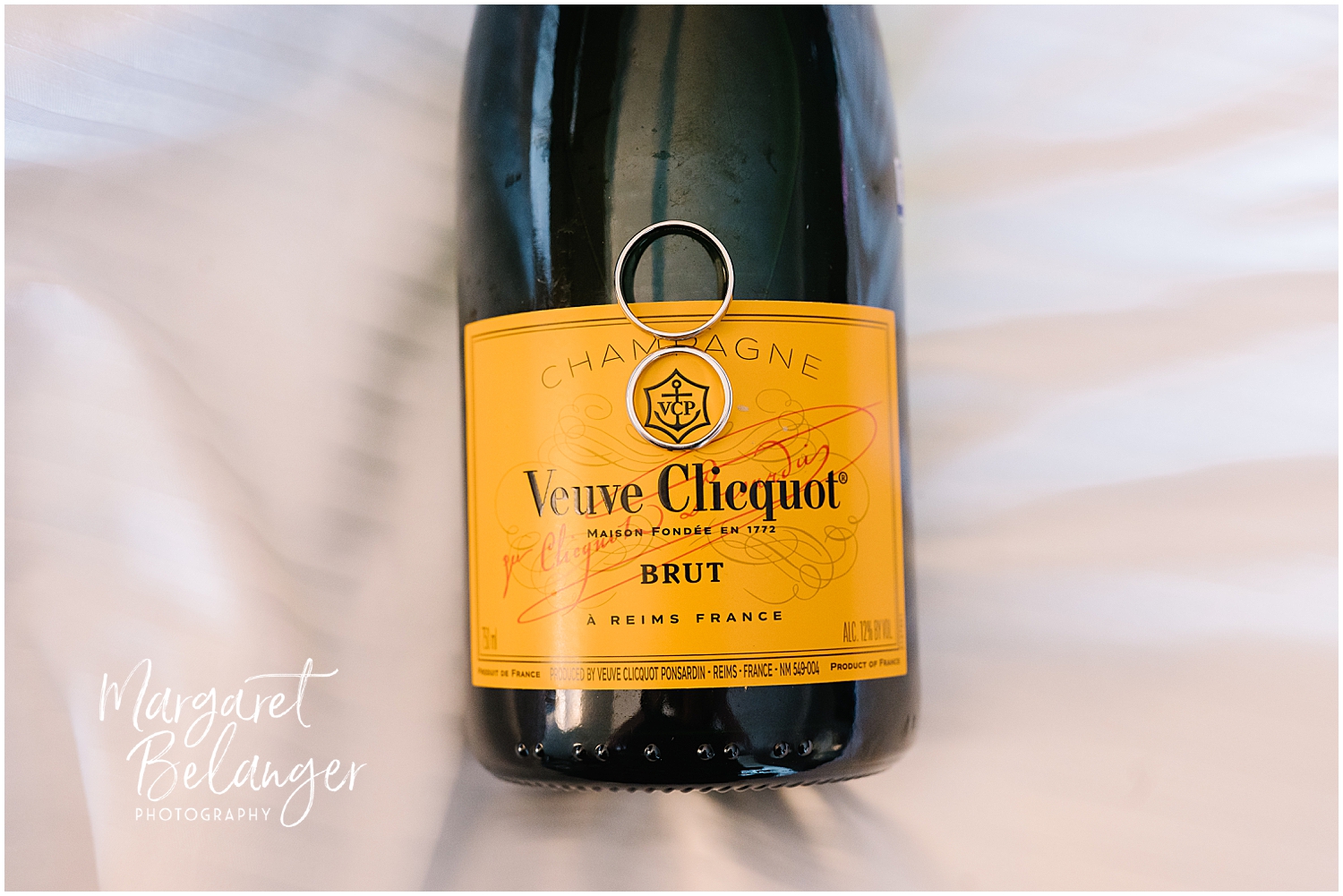 A bottle of veuve clicquot brut champagne with wedding rings placed on the label.