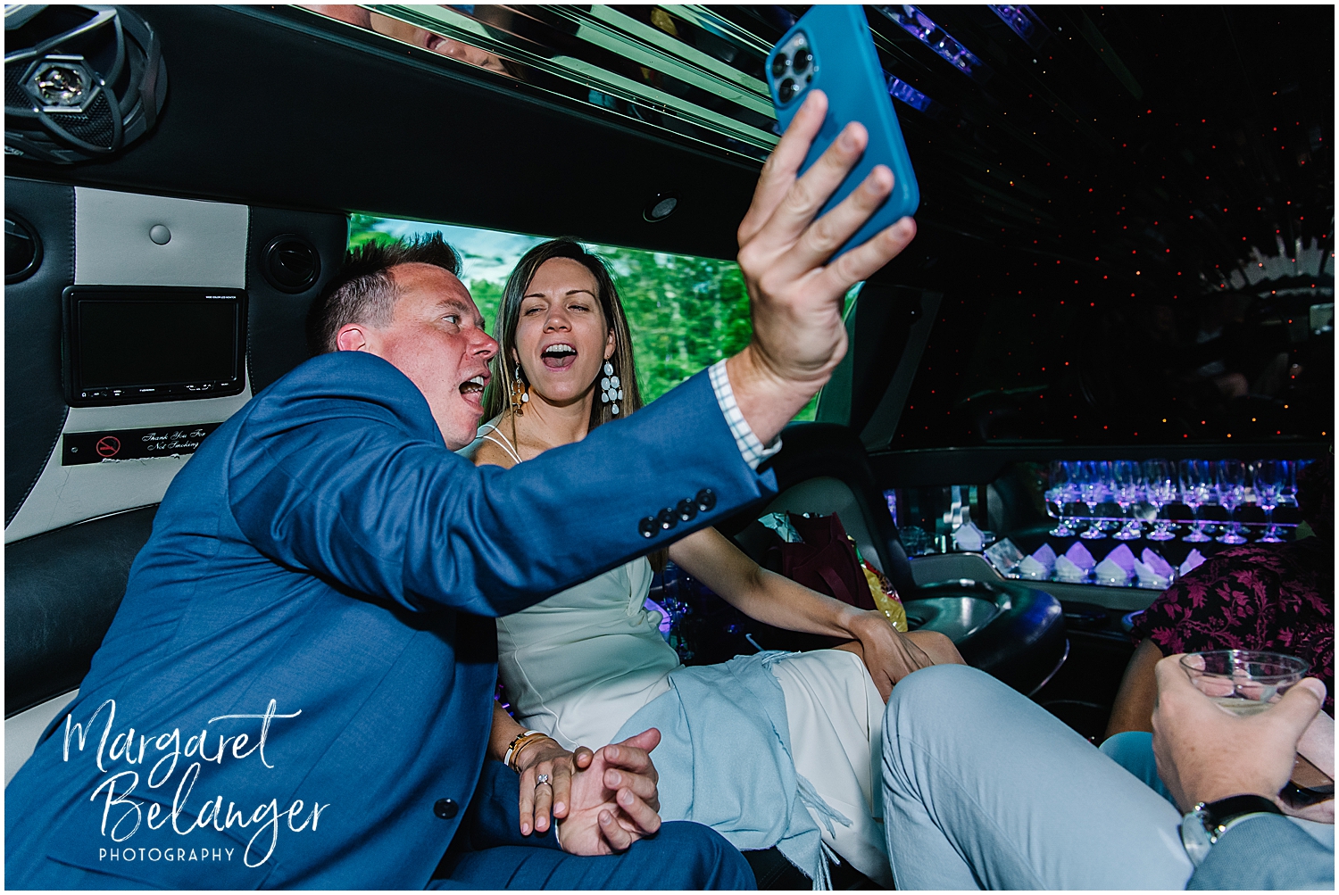 The bride and groom sing along to music while riding in a limousine.