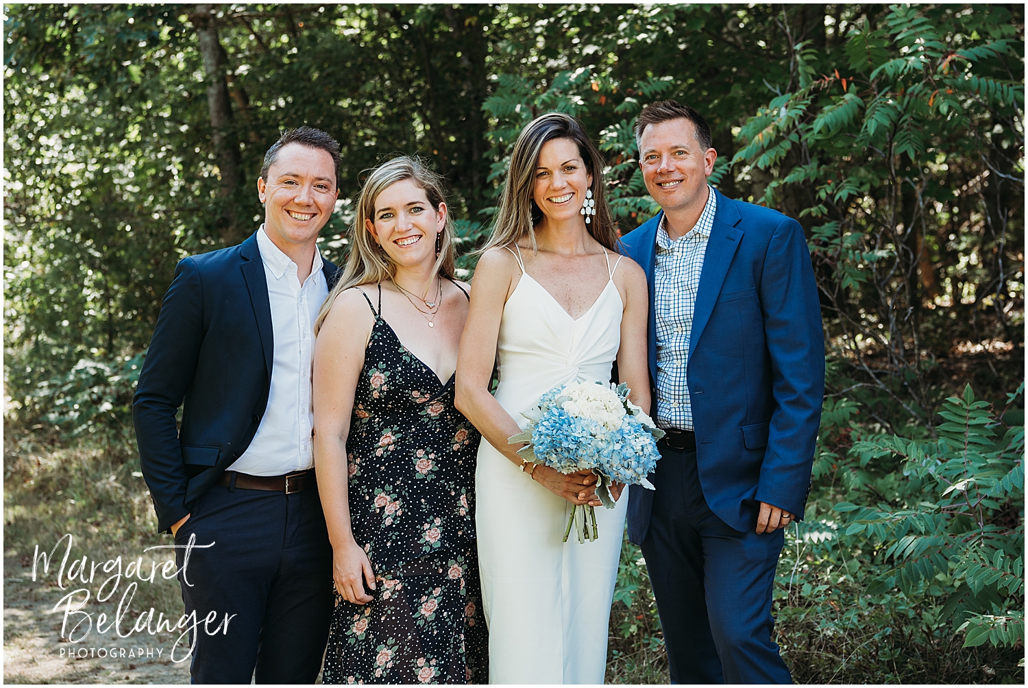 Four people posing for a photo outdoors, with the bride holding a bouquet of flowers.