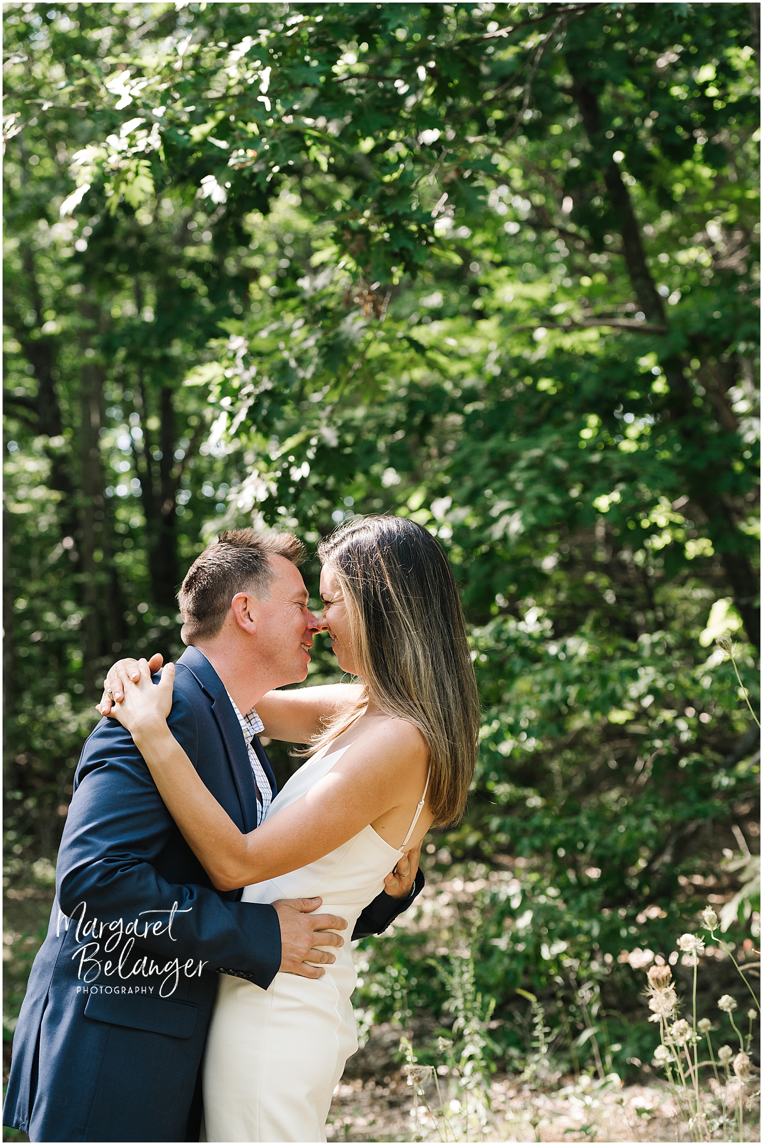 A couple embracing in a sunlit forest clearing.